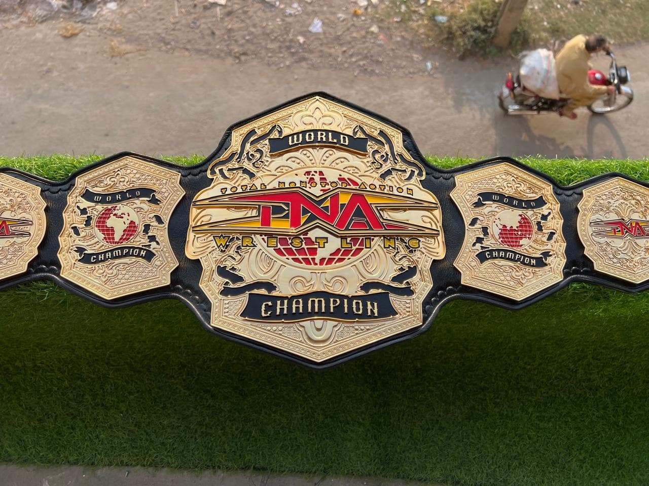 Stacked World Gold Championship Belt laid flat, showing the centre plate and side plates on a black leather strap